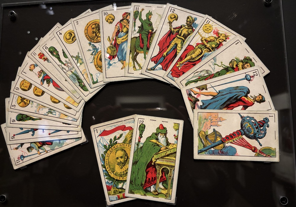 Jeu de cartes inspiré par les aventures de Don Quichotte. Sur les deux cartes du bas, on voit représenté (à gauche) le portrait médaillon de Miguel Cervantès. La carte à droite représente 